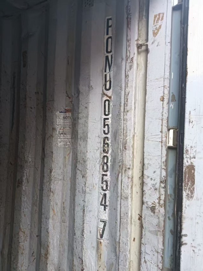 Close-up of a container door and corner post showing surface rust, patched paint and the stencilled container identification number.